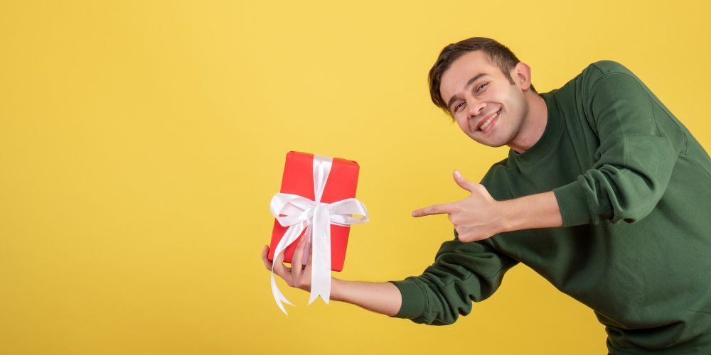 front-view-happy-young-man-pointing-at-gift-on-yellow